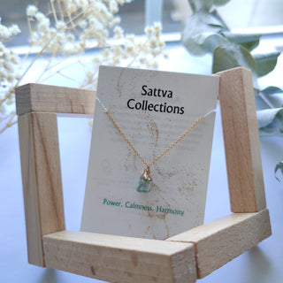 Necklace on a 'Sattva Collections' card with a wooden stand, white flowers in the background