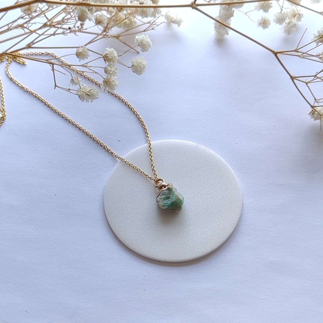 Necklace with a green pendant on a white surface with dried flowers.