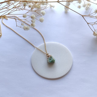 Necklace with a green pendant on a white surface with dried flowers.