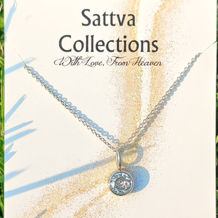 Silver necklace with a round pendant on a 'Sattva Collections' card with grass in the background