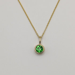 Gold necklace with a green gemstone pendant on a light gray background