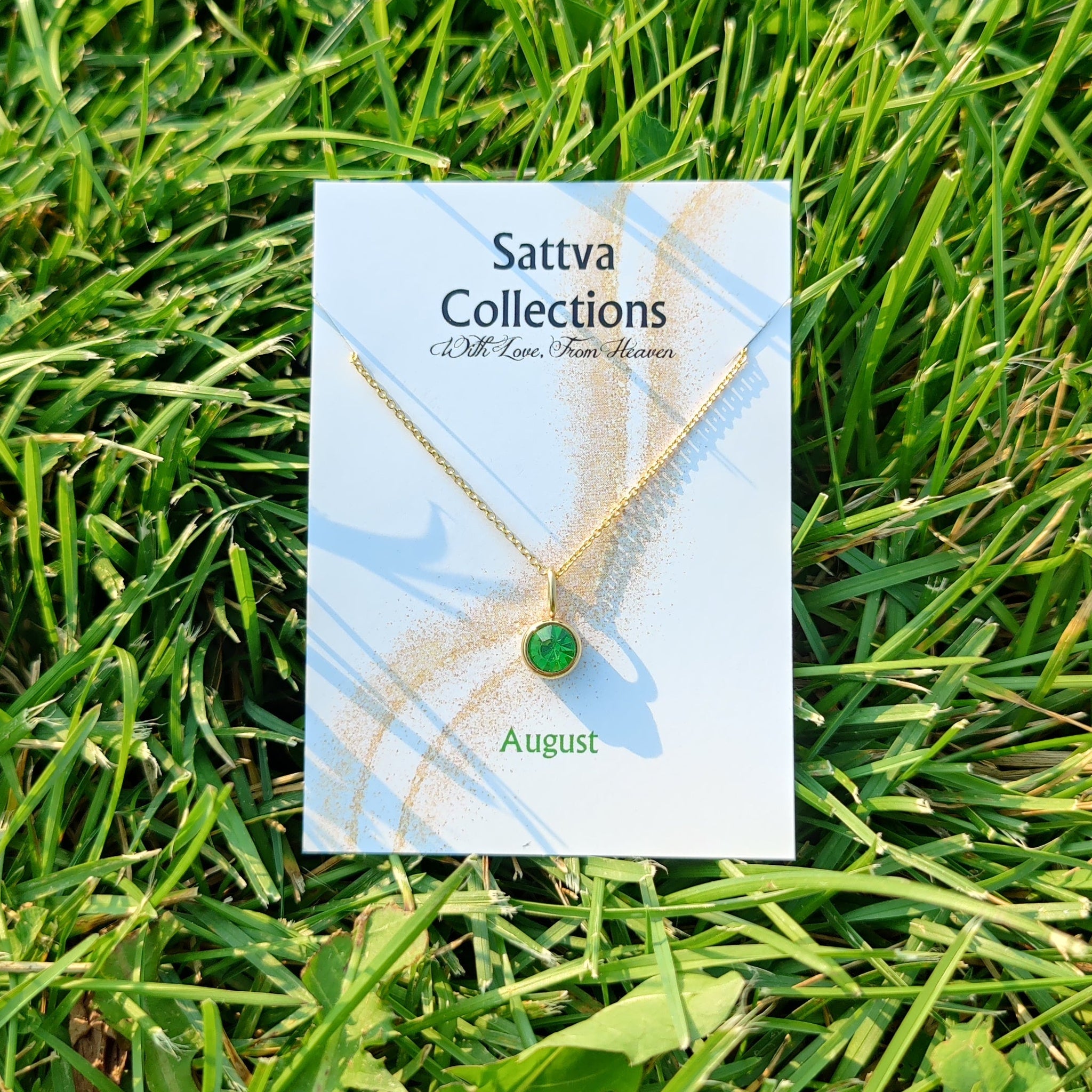 Sattva Collections necklace card with a green gemstone on grass