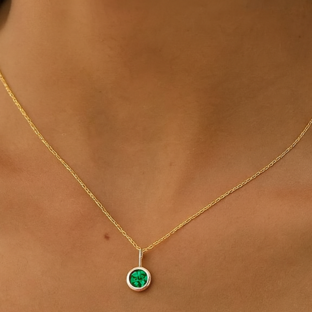 Gold necklace with a green gemstone pendant on a person's neck.