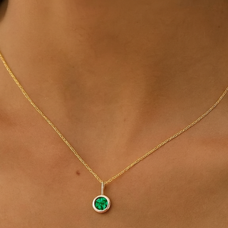 Gold necklace with a green gemstone pendant on a person's neck.