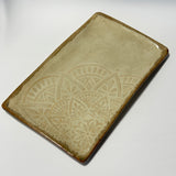 A rectangular ceramic serving platter with rounded corners, featuring a glossy brown border and a raised cream-colored mandala pattern on one half, set against a plain white background.