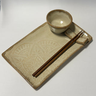 A rectangular ceramic serving tray with embossed geometric patterns, a small matching bowl, chopsticks, and a chopstick rest, photographed on a plain light background.
