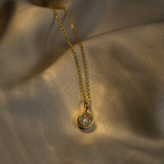 Gold necklace with a diamond pendant on a beige fabric background