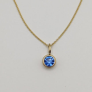 Gold necklace with a blue gemstone pendant on a light gray background