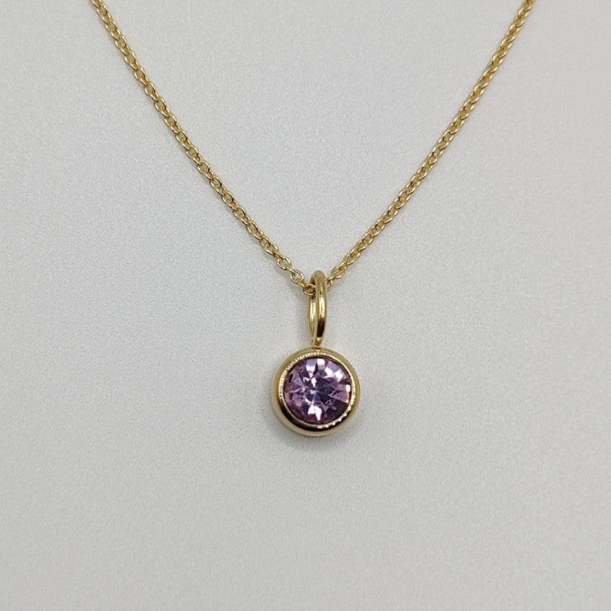 Gold necklace with a pink gemstone pendant on a light gray background
