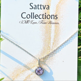 Necklace with a purple gemstone on a 'Sattva Collections' card in grass