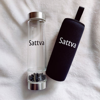 Clear glass pepper grinder and black carrying case with 'Sattva' branding on a white fabric background