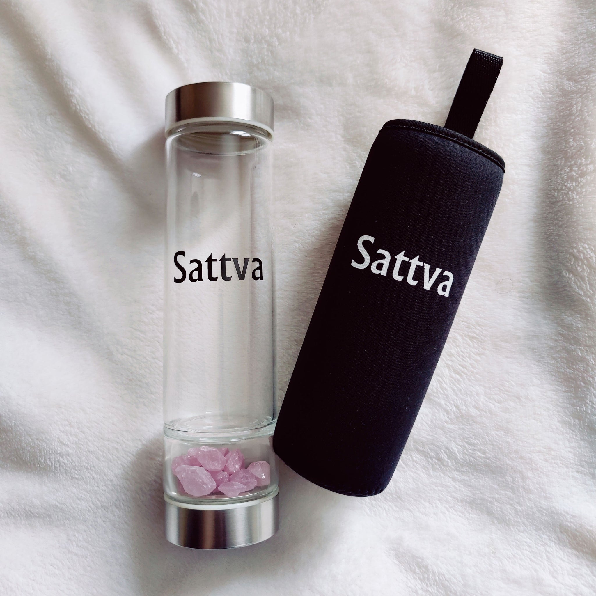 Clear glass bottle with silver cap and black sleeve labeled 'Sattva' on a white fabric background