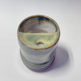 A handmade ceramic planter with a unique asymmetrical half-sloped rim and a small drainage hole, featuring a glossy glaze with blue, green, and brown earthy tones on a white background.