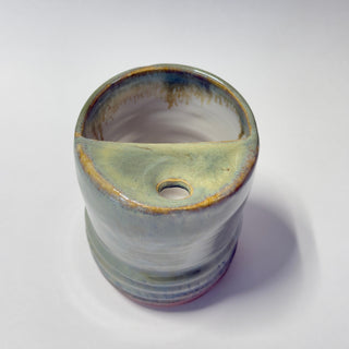 A handmade ceramic planter with a unique asymmetrical half-sloped rim and a small drainage hole, featuring a glossy glaze with blue, green, and brown earthy tones on a white background.