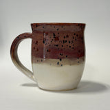 A handmade ceramic mug with a glossy glaze, featuring a gradient design that transitions from a dark reddish-brown speckled top to a warm off-white at the bottom, set against a plain light gray background.