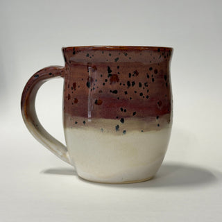 A handmade ceramic mug with a glossy glaze, featuring a gradient design that transitions from a dark reddish-brown speckled top to a warm off-white at the bottom, set against a plain light gray background.