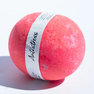 Pink bath bomb with a white band labeled 'Antistress' on a light purple background