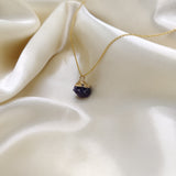 Gold necklace with a purple pendant on a beige fabric background