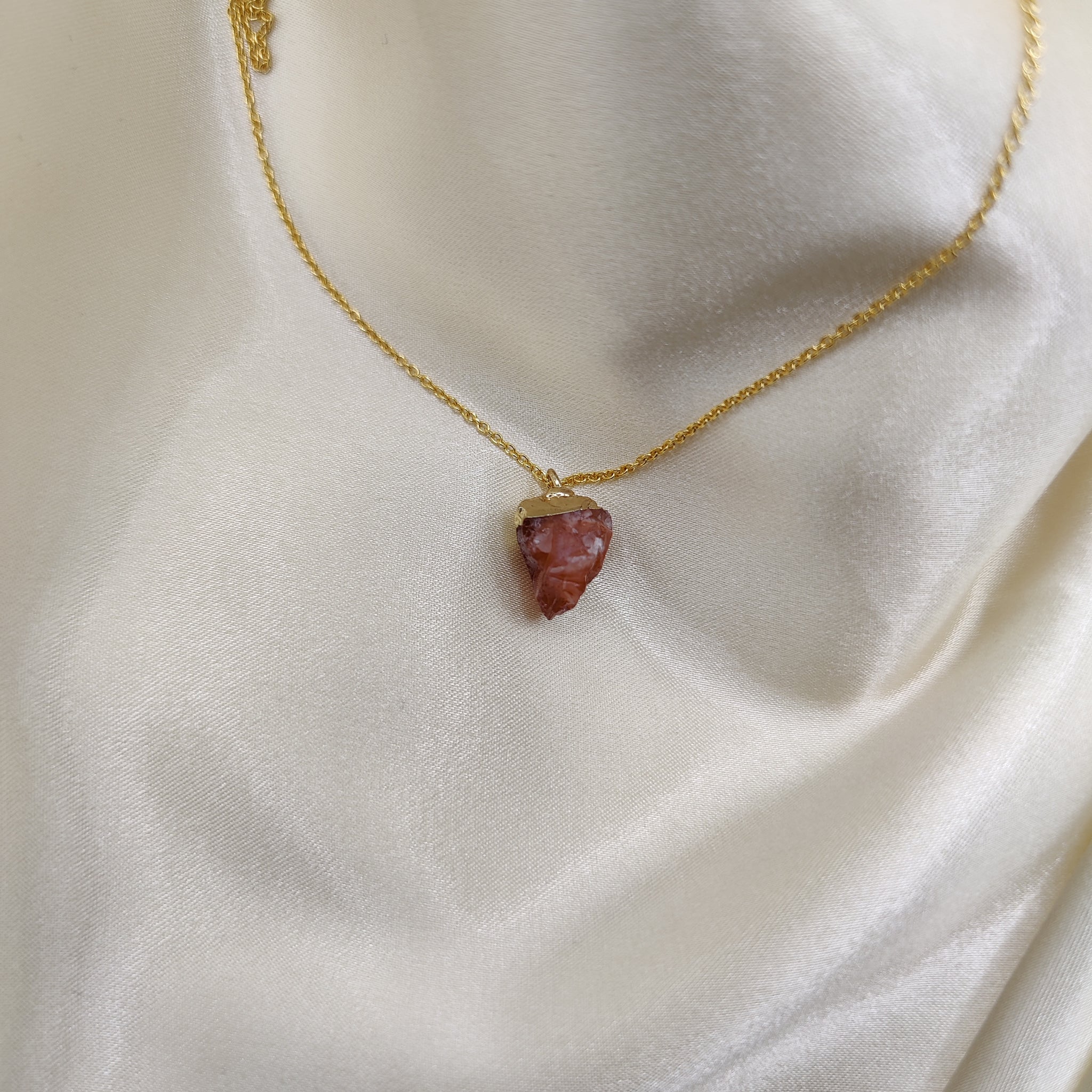 Gold necklace with a red stone pendant on a white fabric background