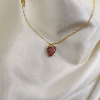 Gold necklace with a red stone pendant on a white fabric background