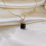 Gold necklace with a black pendant on a white satin background