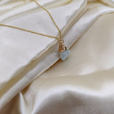 Gold necklace with a blue pendant on a white fabric background