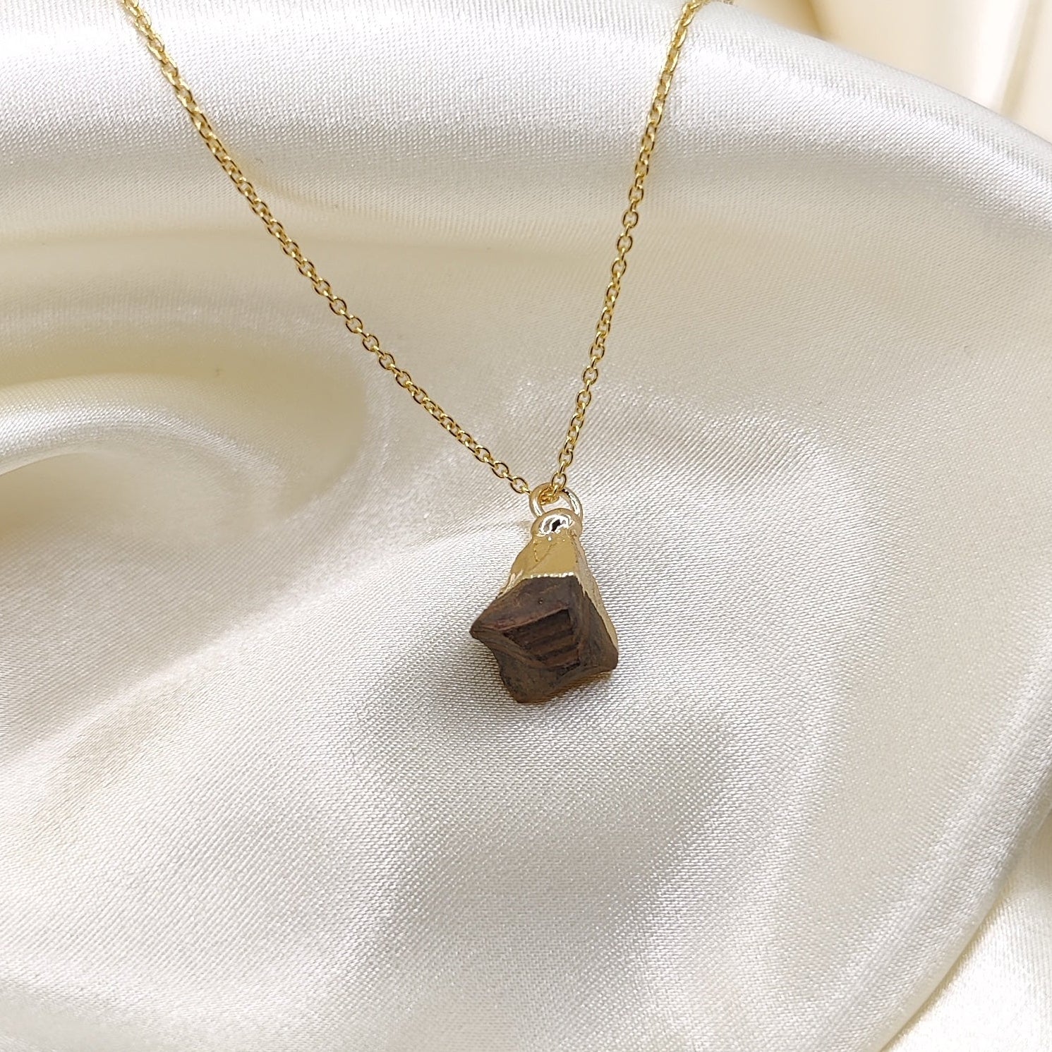 Gold necklace with a triangular pendant on a white fabric background