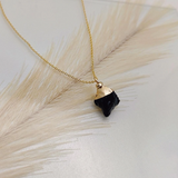 Necklace with a black pendant and gold chain on a light background