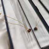 Gold necklace with a brown pendant on a white fabric background