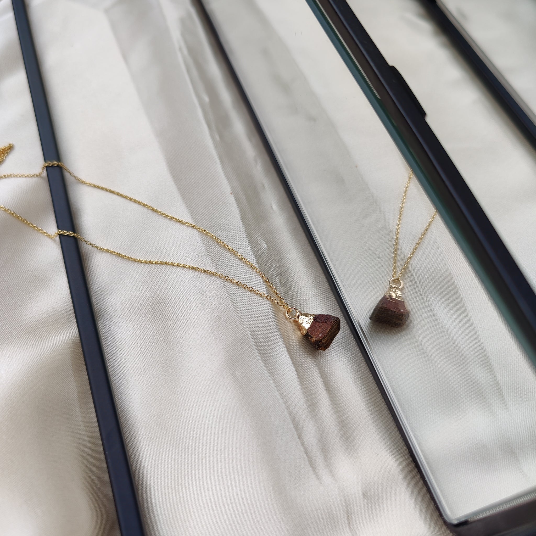 Gold necklace with a brown pendant on a white fabric background