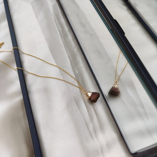 Gold necklace with a brown pendant on a white fabric background