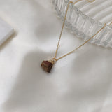 Gold necklace with a brown pendant on a white fabric background