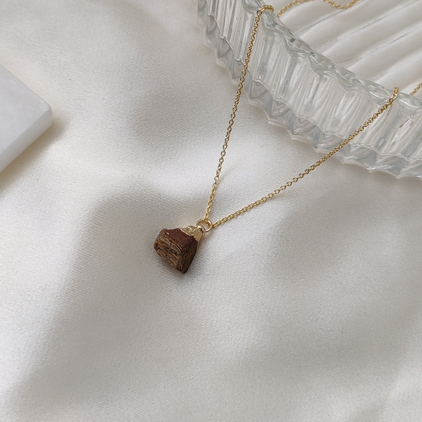 Gold necklace with a brown pendant on a white fabric background