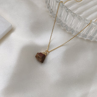 Gold necklace with a brown pendant on a white fabric background