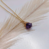 Gold necklace with a purple gemstone pendant on a light background