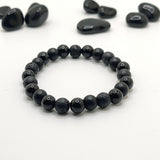 Black beaded bracelet on a white background with scattered black stones.