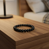 Black beaded bracelet on a white background with scattered black stones.