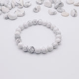 White beaded bracelet on a light gray background with scattered white stones.