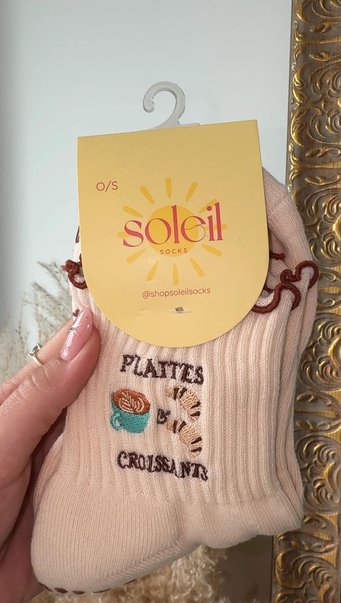 Beige sock with text and graphics, held by a hand against a decorative gold frame.