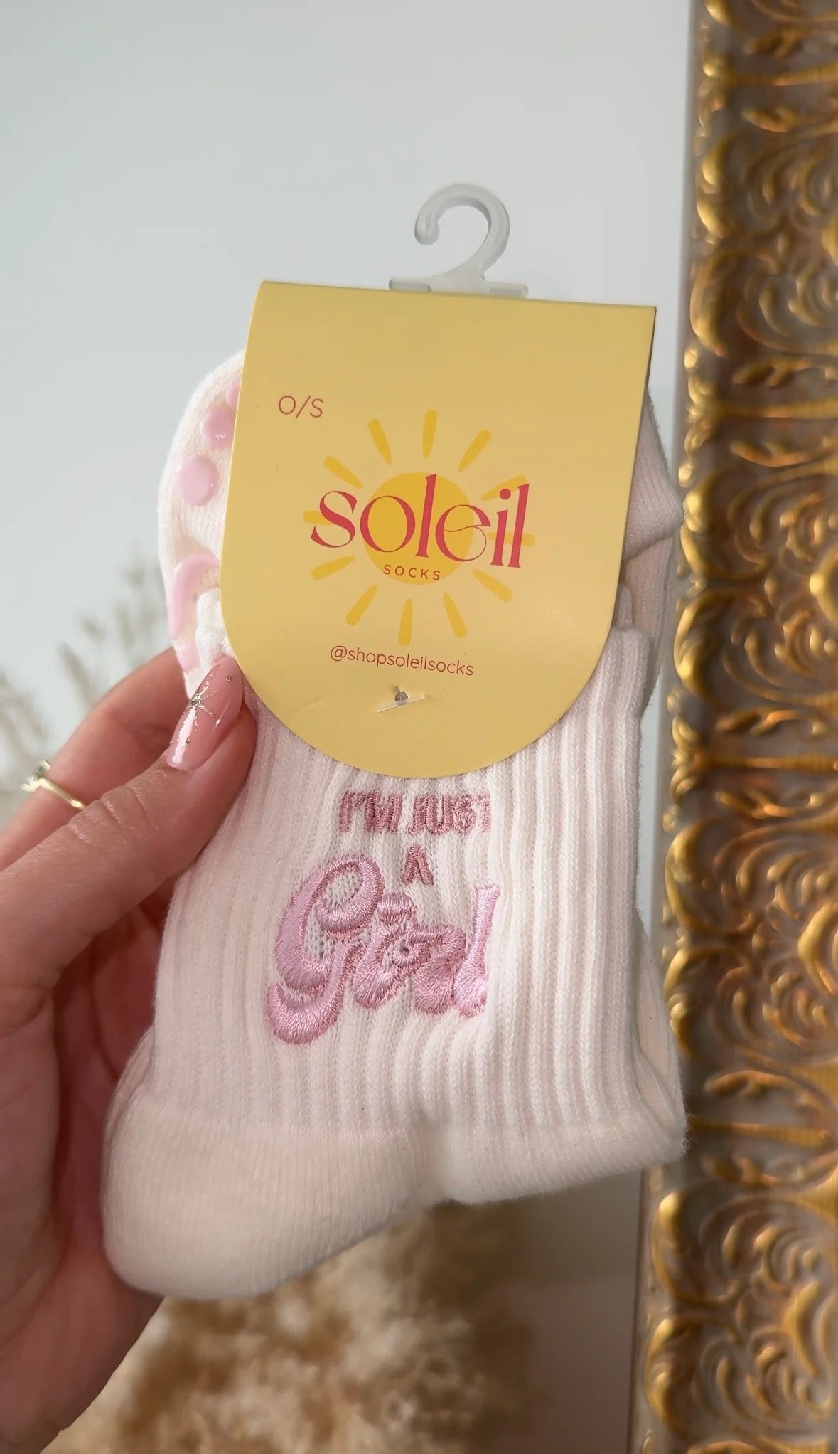 White sock with pink text held by a hand against a decorative mirror background