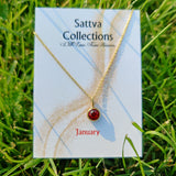 Gold necklace with a red gemstone on a 'Sattva Collections' card in grass