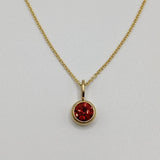 Gold necklace with a red gemstone pendant on a light gray background