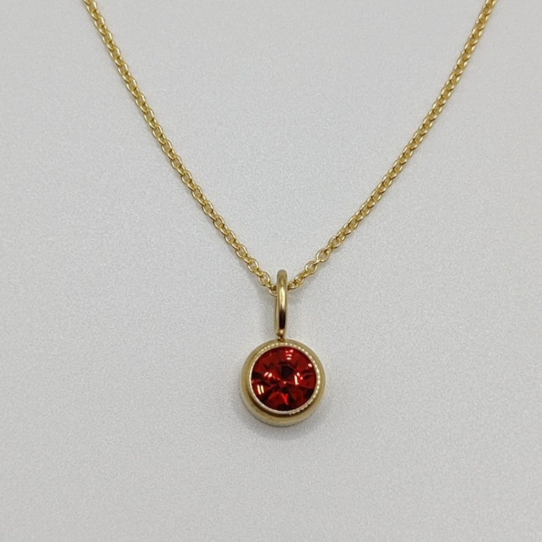 Gold necklace with a red gemstone pendant on a light gray background