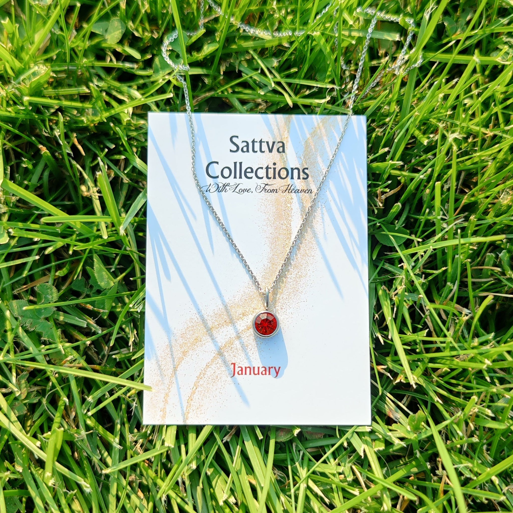 Necklace with a red pendant on a 'Sattva Collections' card lying on grass