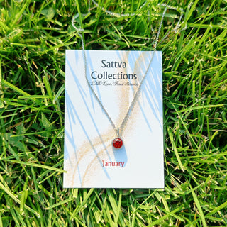 Necklace with a red pendant on a 'Sattva Collections' card lying on grass