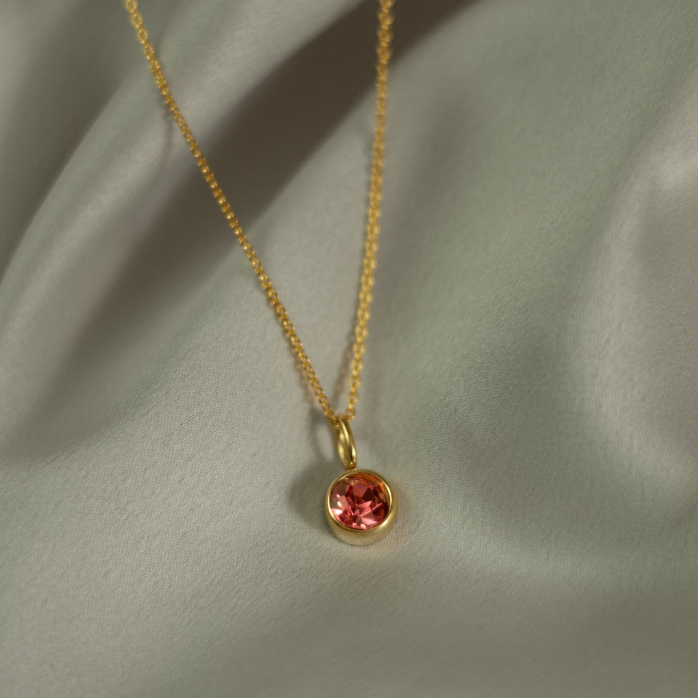 Gold necklace with a red gemstone pendant on a light green fabric background