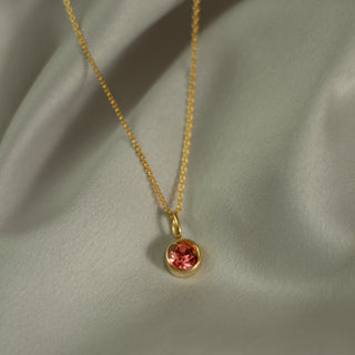 Gold necklace with a red gemstone pendant on a light green fabric background