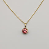 Gold necklace with a pink gemstone pendant on a light gray background