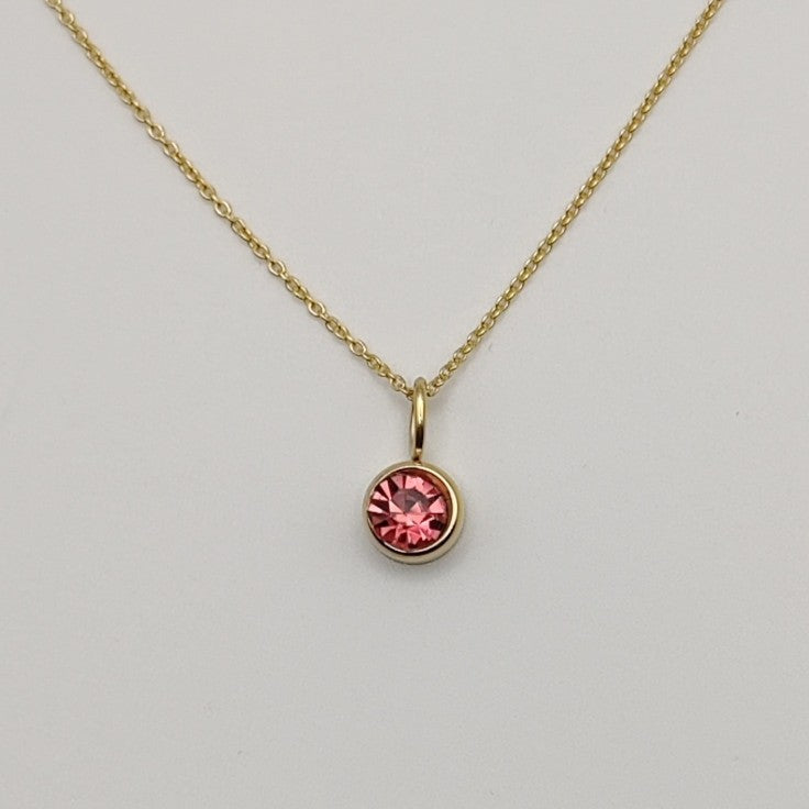 Gold necklace with a pink gemstone pendant on a light gray background
