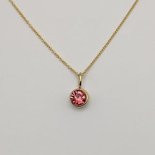 Gold necklace with a pink gemstone pendant on a light gray background